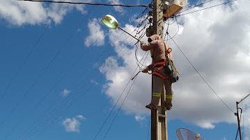 Foto de um homem trocando a lampada de um poste.